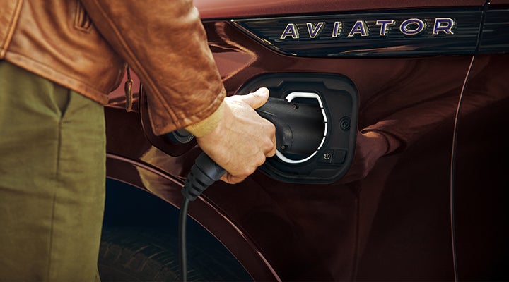 A hand is shown plugging a charger into the charging port of a 2023 Lincoln Aviator® Plug-in Hybrid model. | Cavalier Lincoln in Chesapeake VA