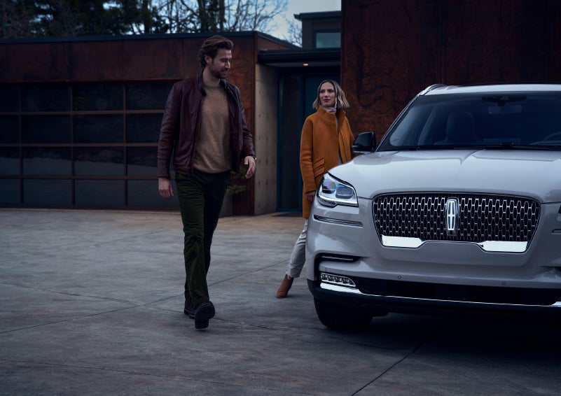 A man and a woman approaching a 2022 Lincoln® Aviator, which illuminates certain lights when they are close