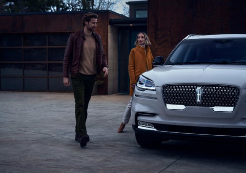 A man and a woman approaching a 2024 Lincoln Aviator® SUV, which illuminates certain lights when they are close | Cavalier Lincoln in Chesapeake VA