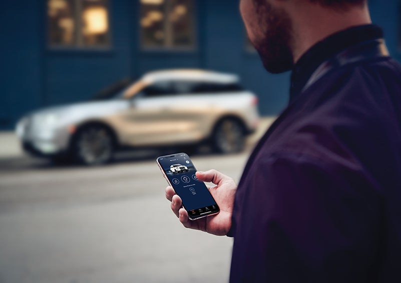 A person is shown interacting with a smartphone to connect to a Lincoln vehicle across the street. | Cavalier Lincoln in Chesapeake VA