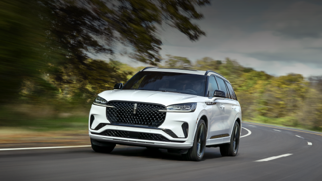 A white 2025 Lincoln Aviator® SUV is being driven down a road lined with trees. | Cavalier Lincoln in Chesapeake VA
