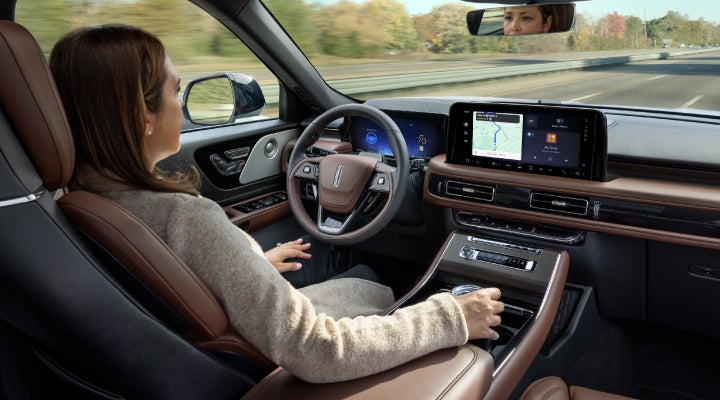 A 2026 Lincoln Aviator® SUV is being driven hands-free on a highway near a forest | Cavalier Lincoln in Chesapeake VA