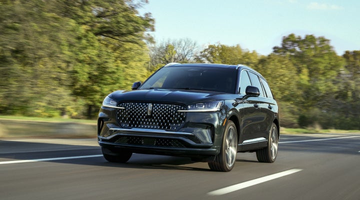 A 2026 Lincoln Black Label™ Aviator® SUV is being driven down a road lined with trees. | Cavalier Lincoln in Chesapeake VA
