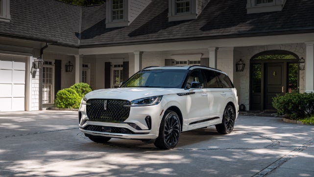 A white 2026 Lincoln Aviator® SUV is parked in the driveway of a luxury home. | Cavalier Lincoln in Chesapeake VA