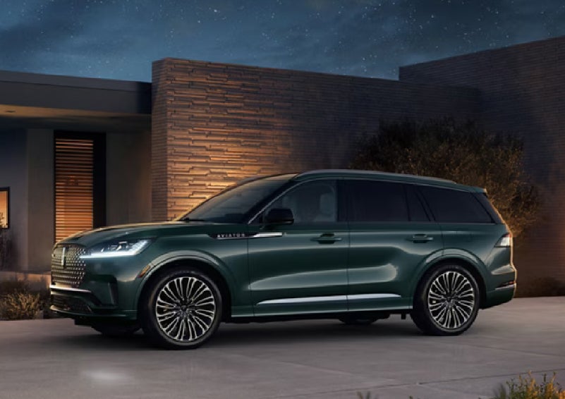 A green 2027 Lincoln Aviator® SUV is parked outside a contemporary home. | Cavalier Lincoln in Chesapeake VA