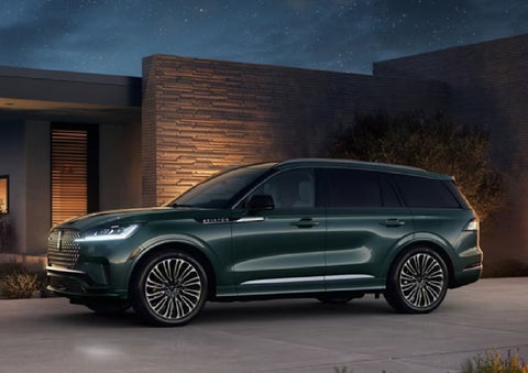 A green 2027 Lincoln Aviator® SUV is parked outside a contemporary home. | Cavalier Lincoln in Chesapeake VA