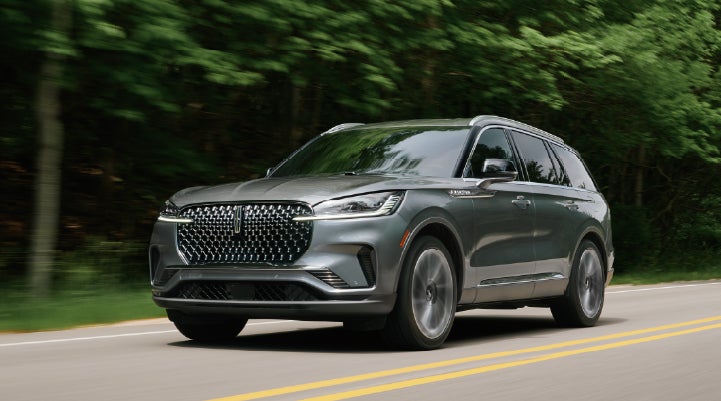 A 2027 Lincoln Aviator® SUV is being driven down a road lined with trees. | Cavalier Lincoln in Chesapeake VA